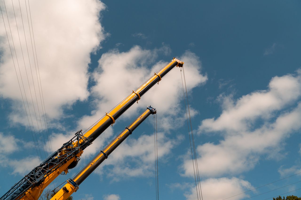 Two yellow construction cranes reaching upward against a clear blue sky with clouds.